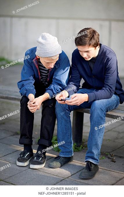 Two teenage boys sitting on bench with mobile phone