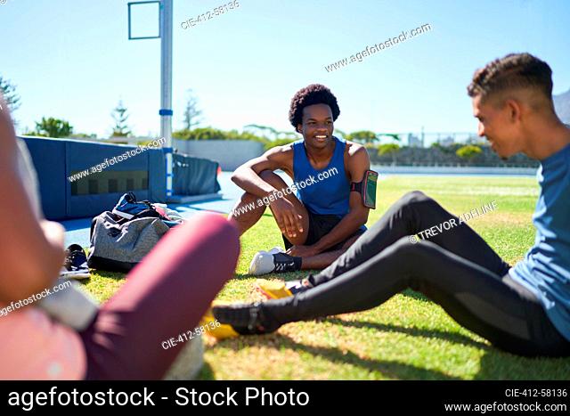 Male runners resting and talking on sunny field