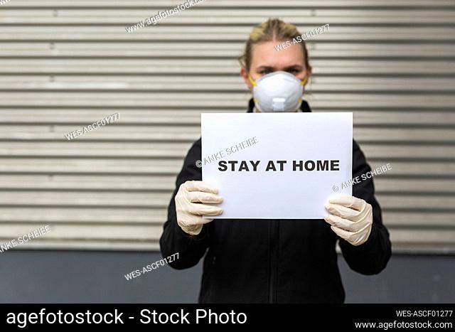 Teenage girl wearing protective mask and gloves holding sign with request 'Stay At Home'