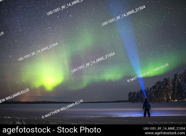 Person under Northern Lights (aurora borealis) display of colourful green and purple in Finnish Lapland, inside Arctic Circle in Finland