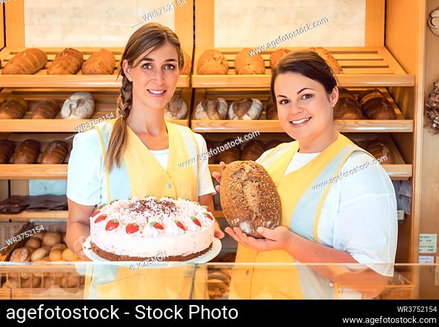 Sales women in bakery with cake and bread showing them to the customer
