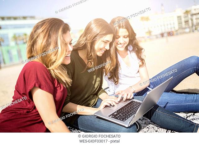 Three happy female friends using a laptop on the beach