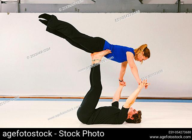 Theme is sports and acreage. A young Caucasian male and female couple practicing acrobatic yoga in a white gym on mats. a man lies on his back and holds a woman...