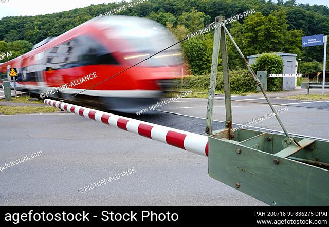 17 June 2020, Rhineland-Palatinate, Imsweiler: A train crosses the Bundesstraße 48 at a level crossing with a closed railway barrier
