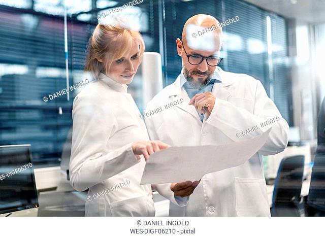 Two technicians wearing lab coats looking at plan