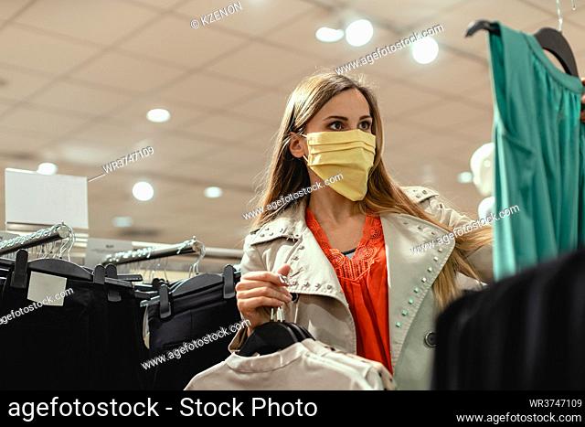Woman shopping in fashion store wearing face mask looking at some clothes
