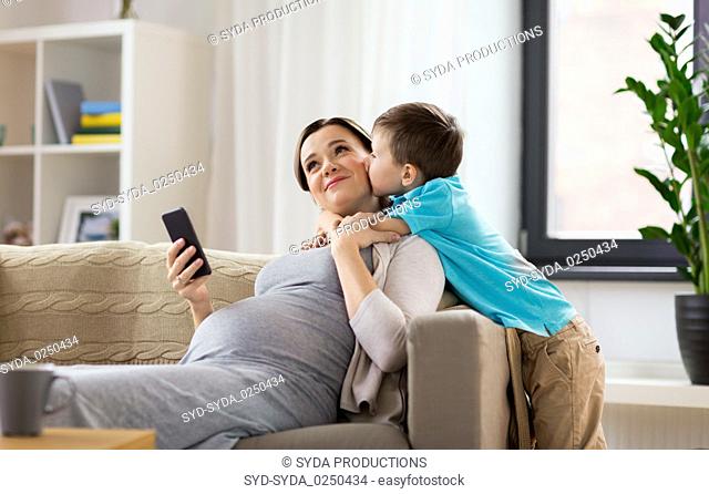 son kissing happy pregnant mother at home
