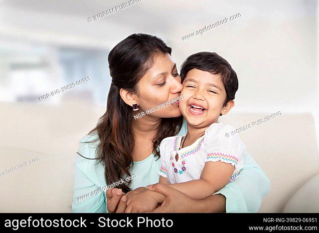 Affectionate mother holding and kissing her daughter on the couch