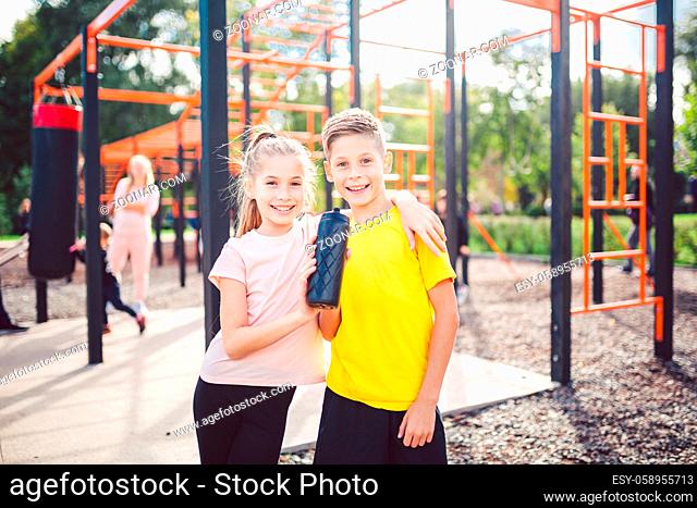Teens children and sports theme. Two kids athletes twins rest and replenish their thirst during workout outdoor gym workout in sunny summer weather