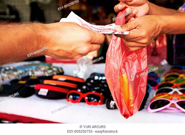 Closeup of money exchanging hands at a market after buying a pair of sunglasses