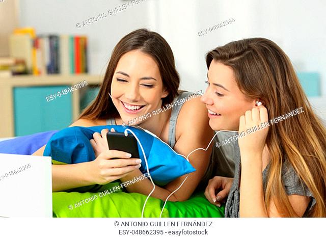 Two teens listening streaming music and sharing earphones in a room