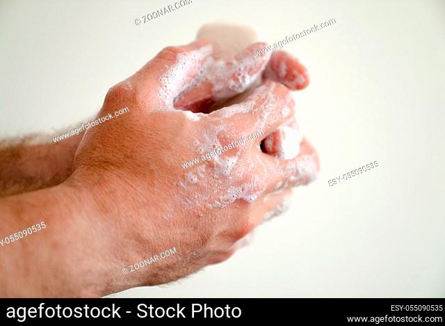 close up of male hands with a bar of soap and soapy suds on a white background