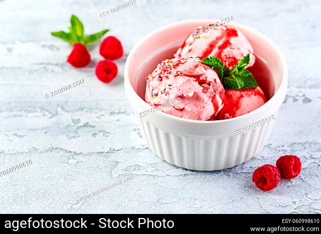 Raspberry ice cream balls with syrup, berries and mint leaves in white bowl