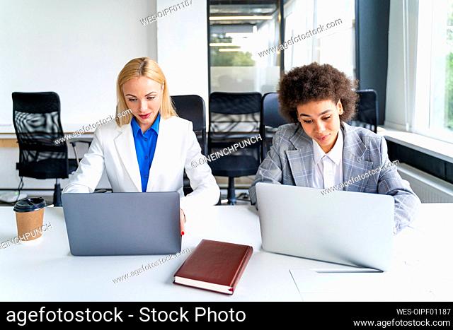Female coworkers using laptops while working in office