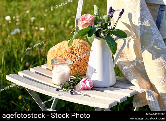 Barefoot walking - utensils such as natural sponge, salt, lavender, petals for natural foot care on a white garden chair in the countryside
