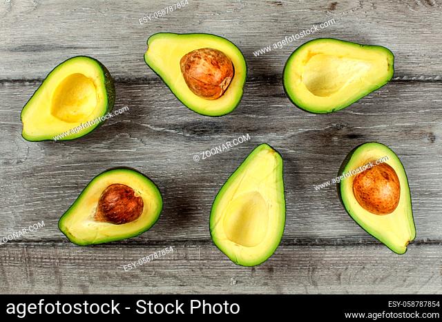 Tabletop view - arranged avocado halves, some of them with the seed, on gray wood desk