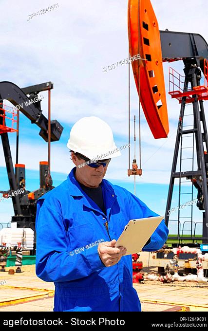 Man working on a tablet with pumpjacks in the background; Alberta, Canada