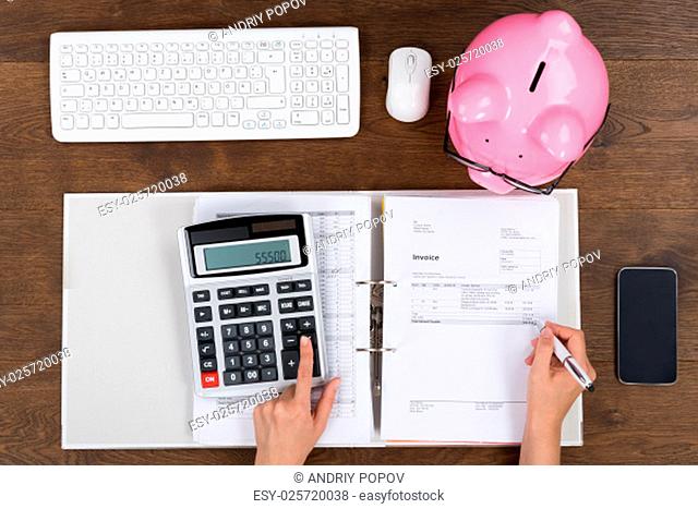 Person Hands Calculating Receipt With Piggybank And Cellphone At Desk