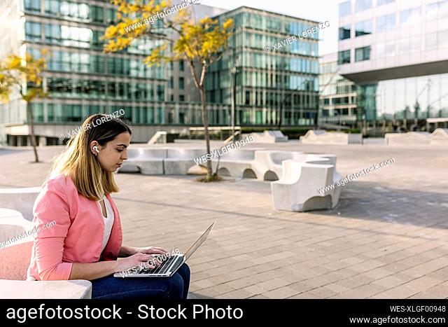 Spain, Barcelona, Young businesswoman using laptop in front of office buildings