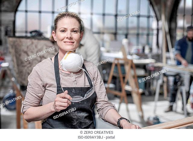 Portrait of craftswoman holding safety goggles in antique restoration workshop