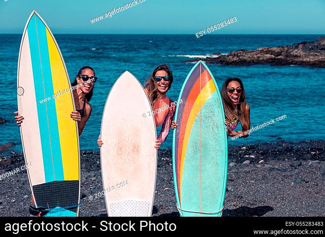 Playful diverse women in sunglasses looking from behind surfing boards standing in row on ocean beach