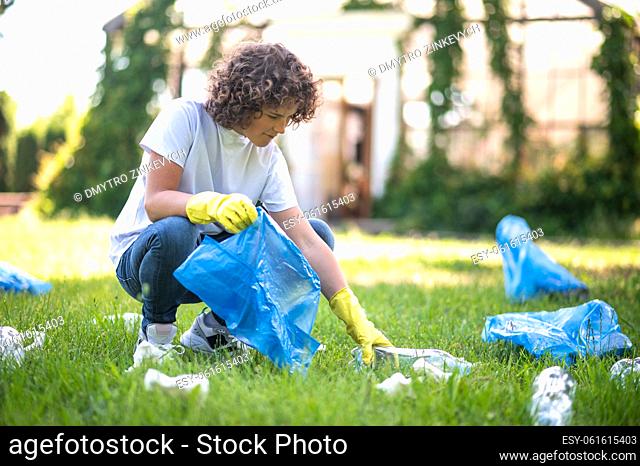 Gathering garbage. Curly-haired teen gathering garbage in the park