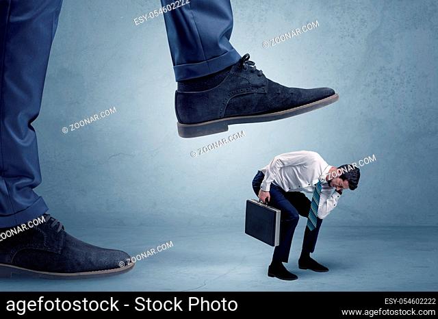 Young small businessman is trampled by a big foot in an empty space