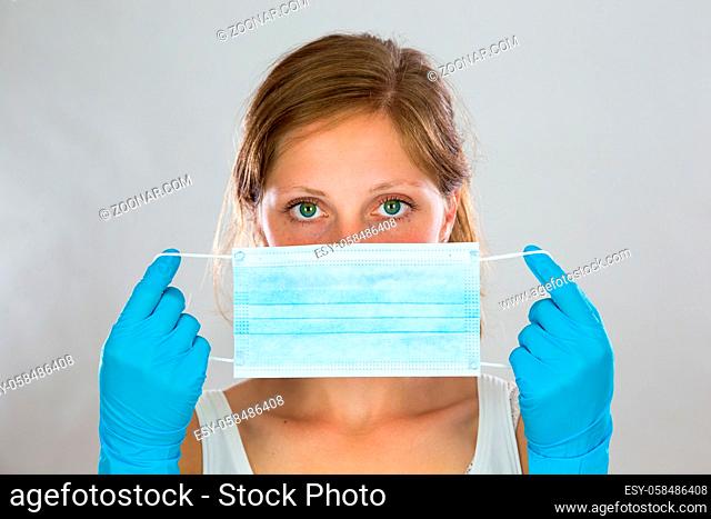Woman stretching ear loops of blue surgical mask as she is attaching it to her face. Nurse protecting her respiratory system against coronavirus