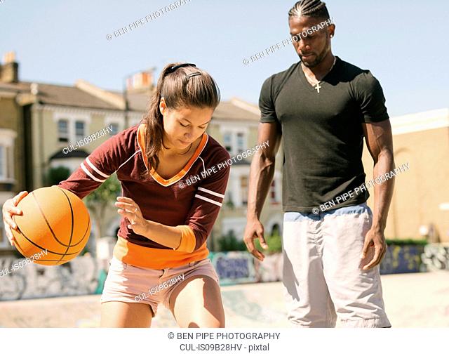 Woman and young man practising basketball in skatepark