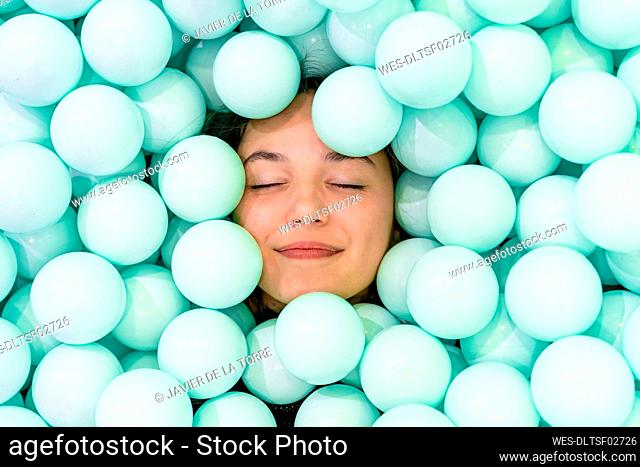 Smiling woman with eyes closed amidst blue balls