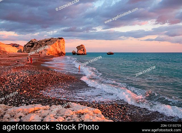 Paphos, Cyprus - November 24, 2018: People enjoy themselves at the beach againt the Petra tou Romiou rocks bathed in afternoon light, in Paphos, Cyprus