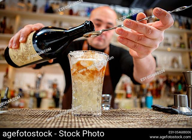 Bartender pouring cocktail into glass at the bar
