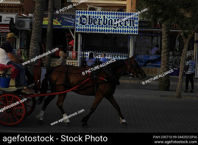 09 July 2023, Spain, Palma: A horse-drawn carriage passes next to the disco ""Oberbayern"" on the beach of Arenal. Photo: Clara Margais/dpa