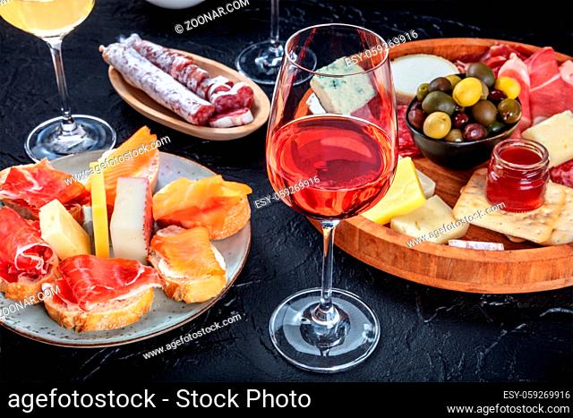 Rose wine and Italian antipasti or Spanish tapas in a bar. Blue cheese, prosciutto di Parma ham, jamon, olives and samon sandwiches