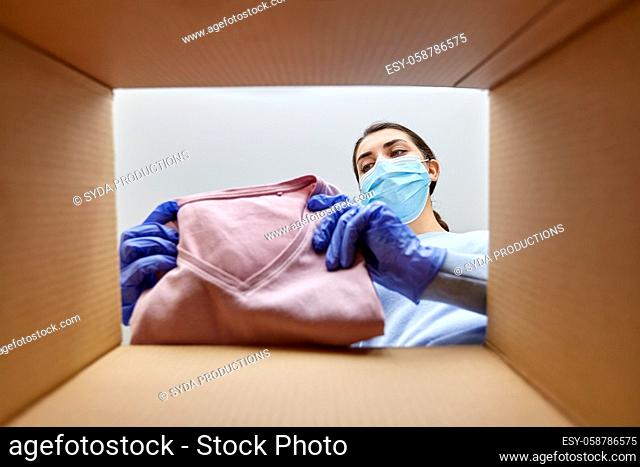 woman in mask opening parcel box with clothes