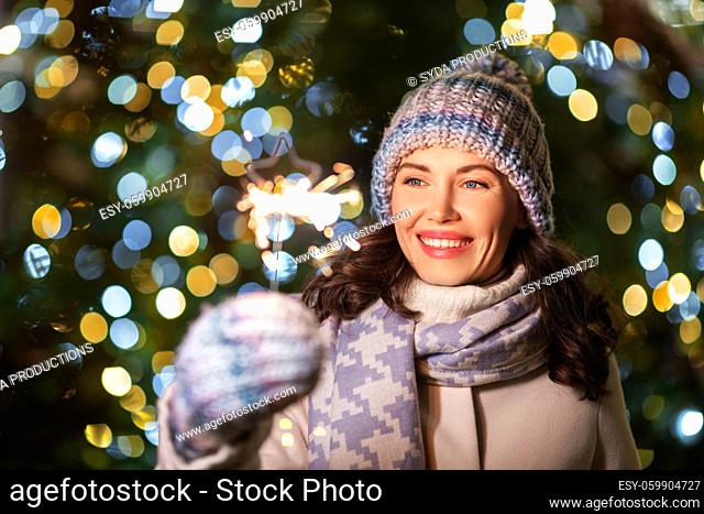 happy woman with sparkler over christmas lights
