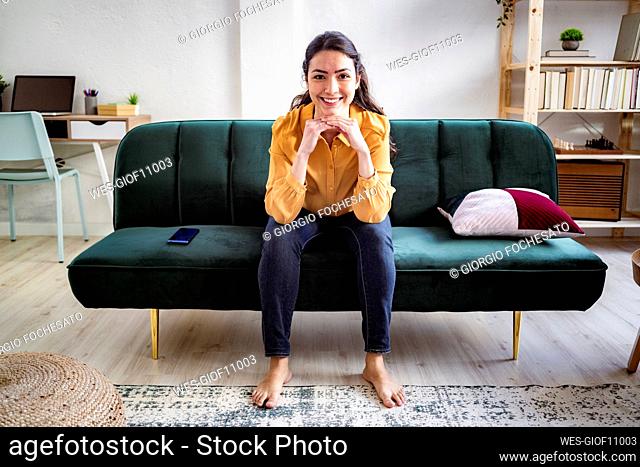 Smiling woman sitting with hand on chin at home