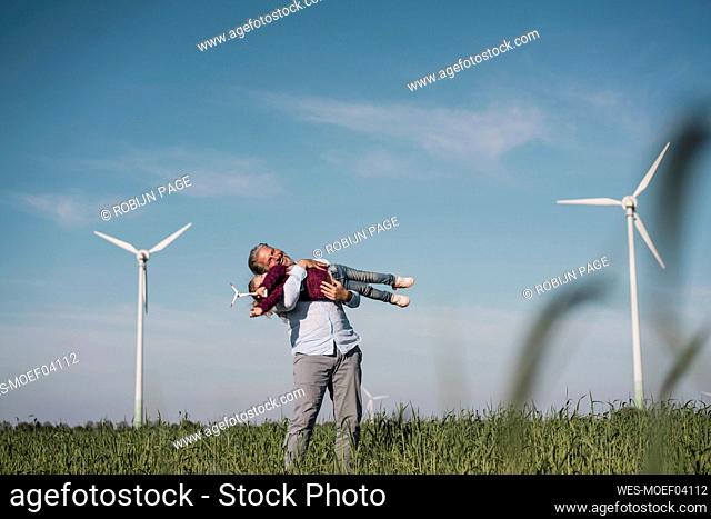 Happy man carrying daughter standing in field on sunny day