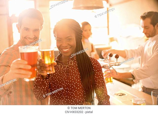 Portrait smiling couple toasting beer glasses at bar