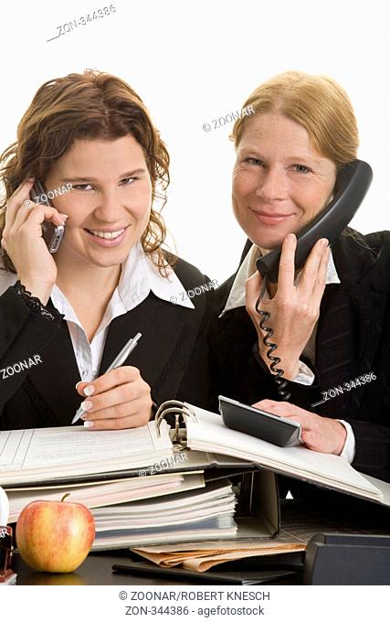 Zwei weibliche Büroangestellte telefonieren zusammen und bearbeiten Akten