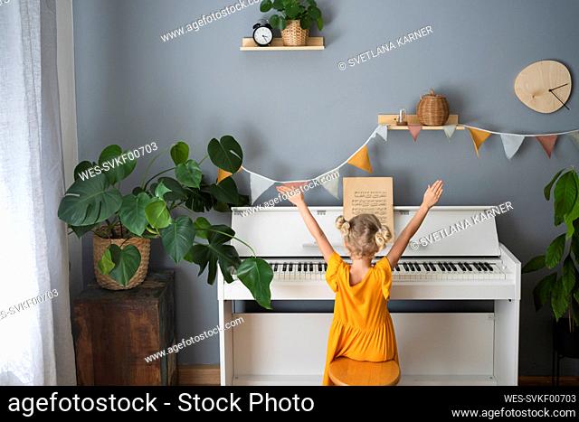 Girl with hands raised sitting by piano at home