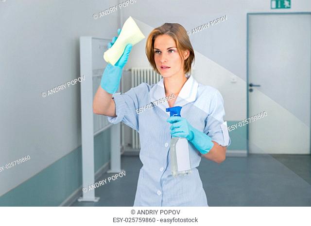 Young Beautiful Female Maid Wiping Glass With Rag In Corridor