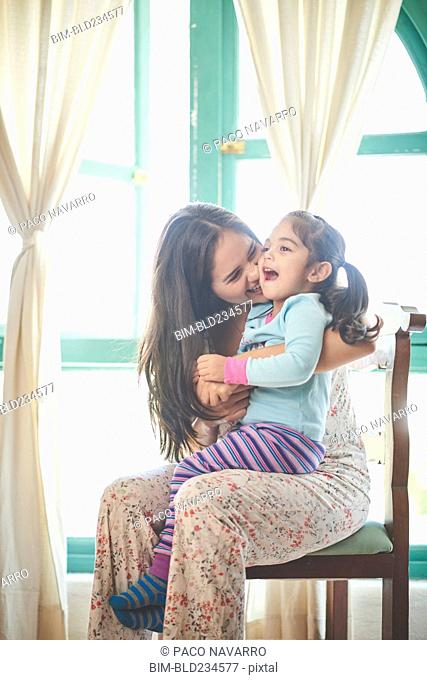 Hispanic mother sitting in chair holding laughing daughter