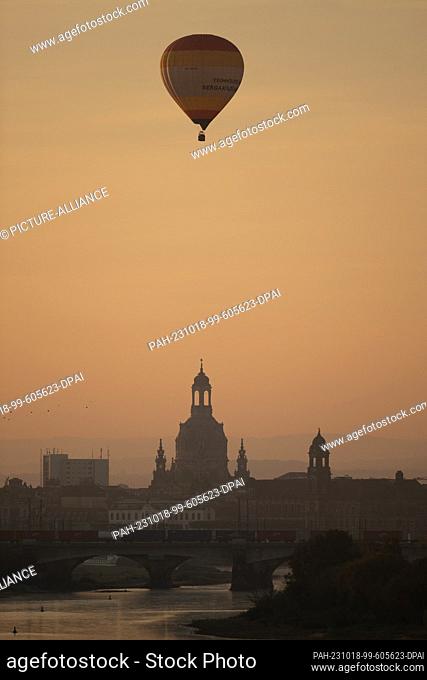 18 October 2023, Saxony, Dresden: A hot air balloon rides over the backdrop of the old town at sunrise. Photo: Sebastian Kahnert/dpa