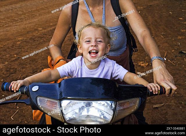 Travel with children's. Mother riding a motorbike with her daughter. Ratanakiri. The protected area of Yeak Lom includes a circular crater-lake