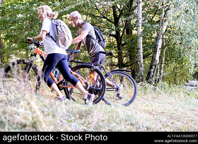 Mature couple with bicycles walking in forest