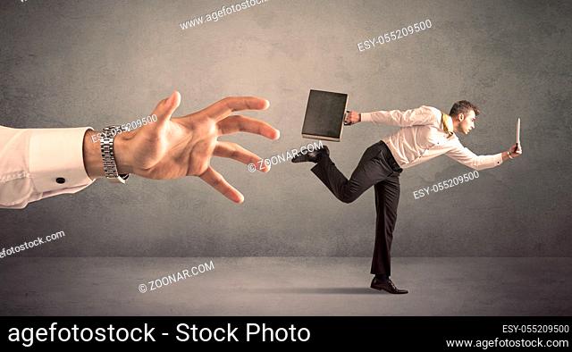 Young miniature businessman running from a big hand with grey background