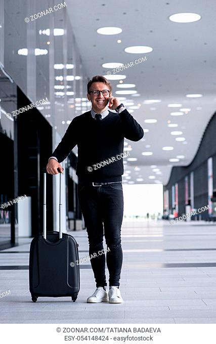 Man walking with wheeled bag at airport terminal and talking on phone
