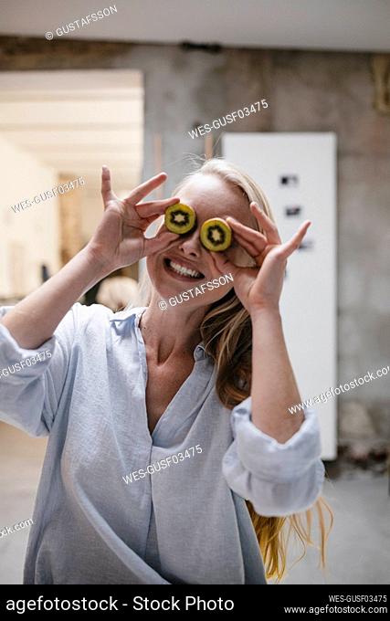 Happy young woman covering her eyes with kiwis