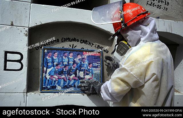 29 May 2020, Peru, Lima: A cemetery worker in a protective suit, at the request of a family, places an older picture of the football club of the man who died of...